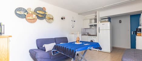 A compact living space with a sofa, a foldable table, a kitchenette, and decorative wall art.