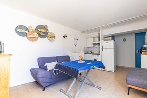 Ein gemütlicher, kompakter Wohnbereich mit Sofa, klappbarem Tisch, Küchenzeile und dekorativen Wandbildern.