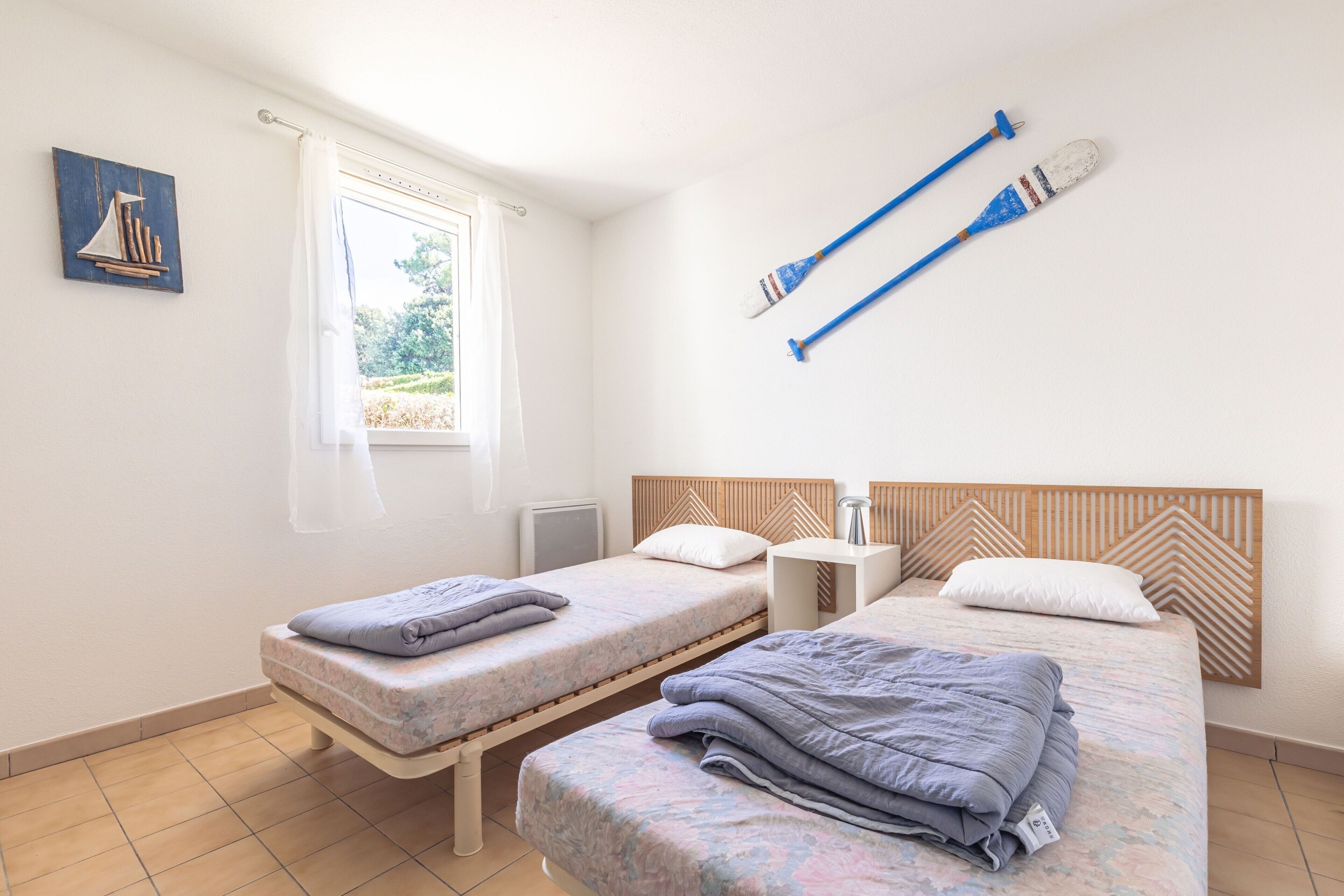 Une chambre avec deux lits, une fenêtre avec des rideaux, un radiateur et un tableau accroché au mur.