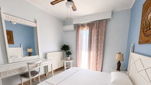 Una camera da letto con un letto, una scrivania, una sedia, un termosifone, una pianta, una finestra con tende e una ventola a soffitto.