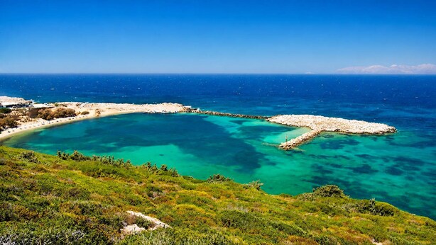 Paesaggio costiero con mare cristallino blu, formazioni rocciose e vegetazione verde.