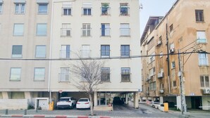 A multi-story building with a parking garage entrance, a tree in front, and several parked cars. - Hayarkon Joie in Tel Aviv-yafo (Tel Aviv)