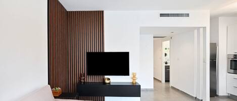 Una sala moderna con un sofá, un televisor de pantalla plana, una mesa consola negra y una cocina al fondo.