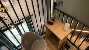 A modern loft-style room with a wooden dining table, a single chair, a small trash bin, and a potted plant. - Epanomi Suites - Modern Living With Garden Retreat (Thermaikos)