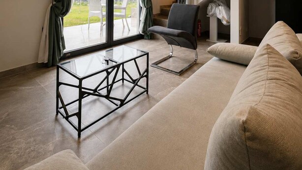 A modern living room with a sofa, a glass coffee table, and a chair. There is a staircase leading to an upper level, and a flat-screen TV mounted on the wall. - Epanomi Suites - Modern Living With Garden Retreat (Thermaikos)