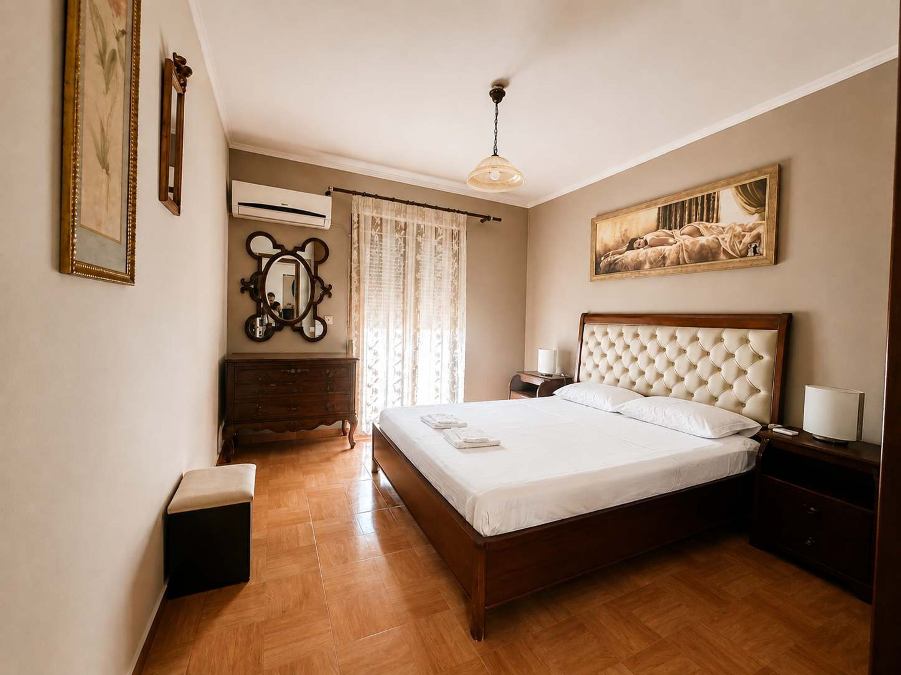 Um quarto com uma cama de madeira, uma cômoda, um espelho, um ar condicionado e um quadro na parede.
