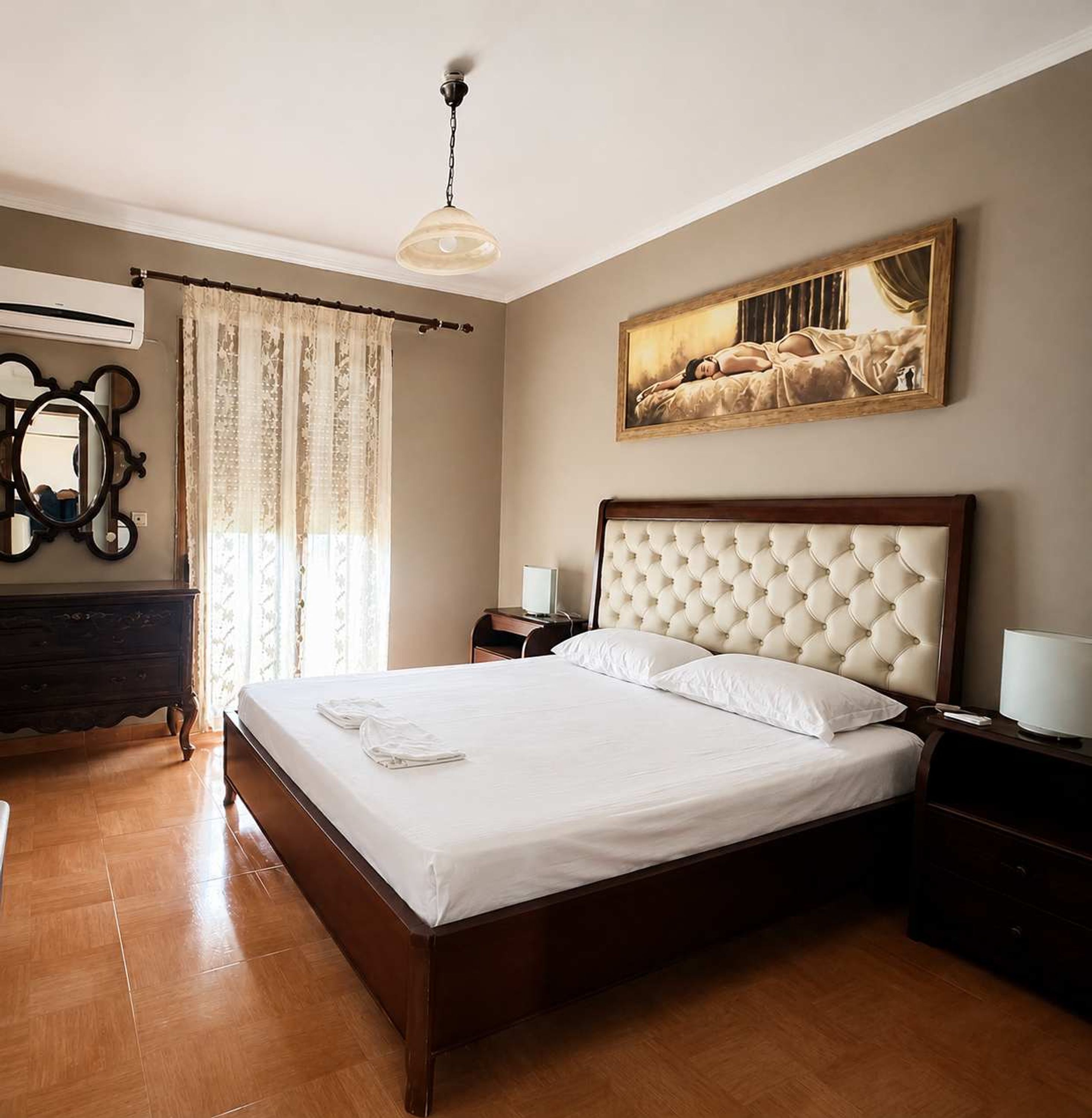 Quarto com cama, penteadeira, espelho, quadro e ventilador de teto.