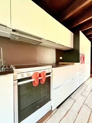 Een keuken met witte kastjes, een fornuis, oven en rode ovenwanten die aan de ovenhandgreep hangen.