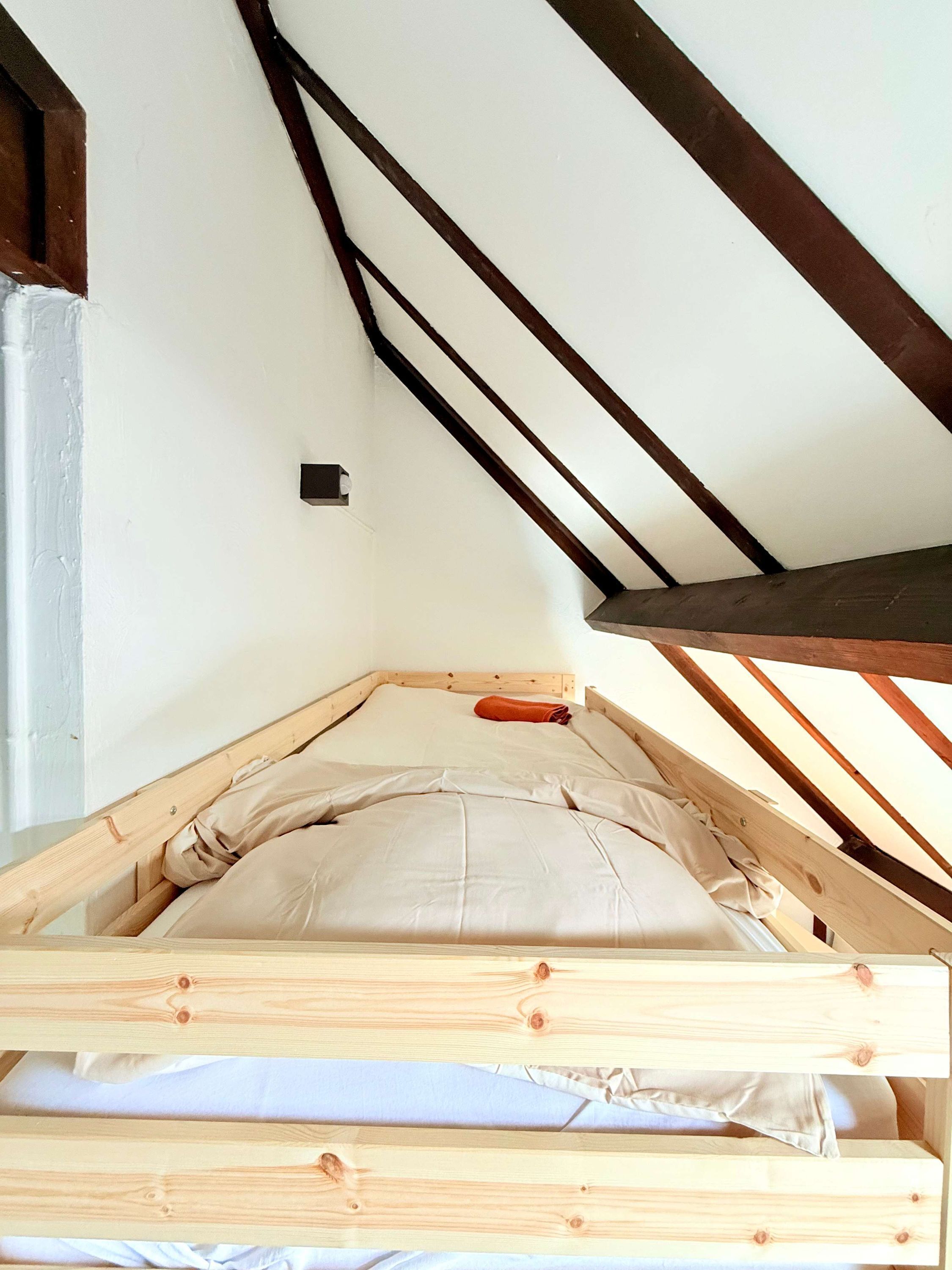 A loft-style bedroom with a sloped ceiling, wooden beams, and a simple bed setup.