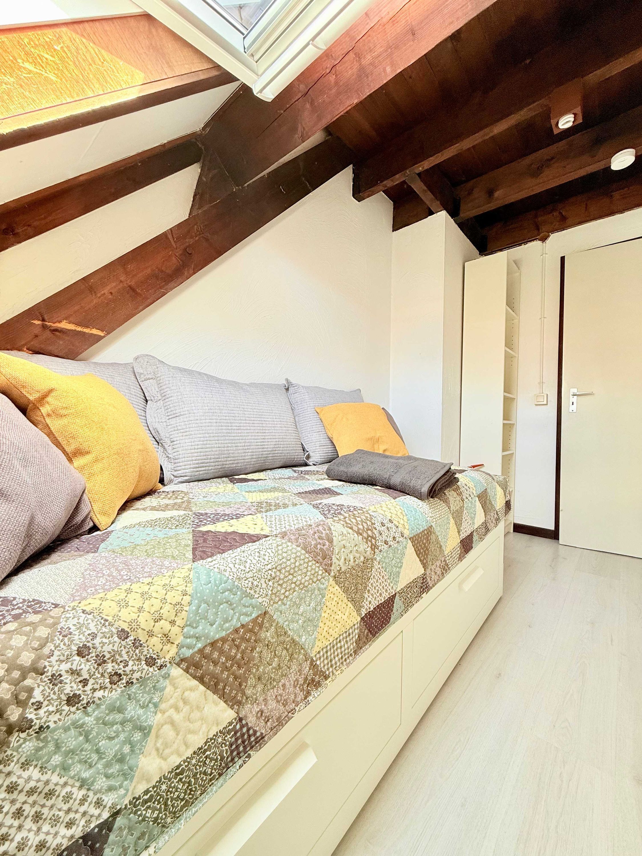 Un dormitorio con techo inclinado, una cama con colcha, un armario y una puerta.