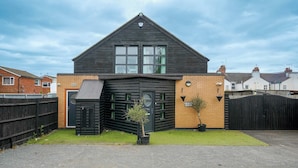 A modern two-story house with a dark exterior, a garage door, and a small front yard with a potted plant. - 6-bedroom Family Haven With Garden in Aylesbury (Aylesbury)
