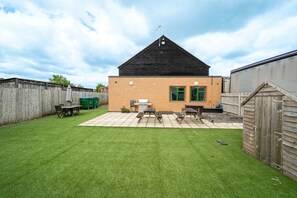 Un jardin avec une terrasse, un barbecue et une clôture en bois.