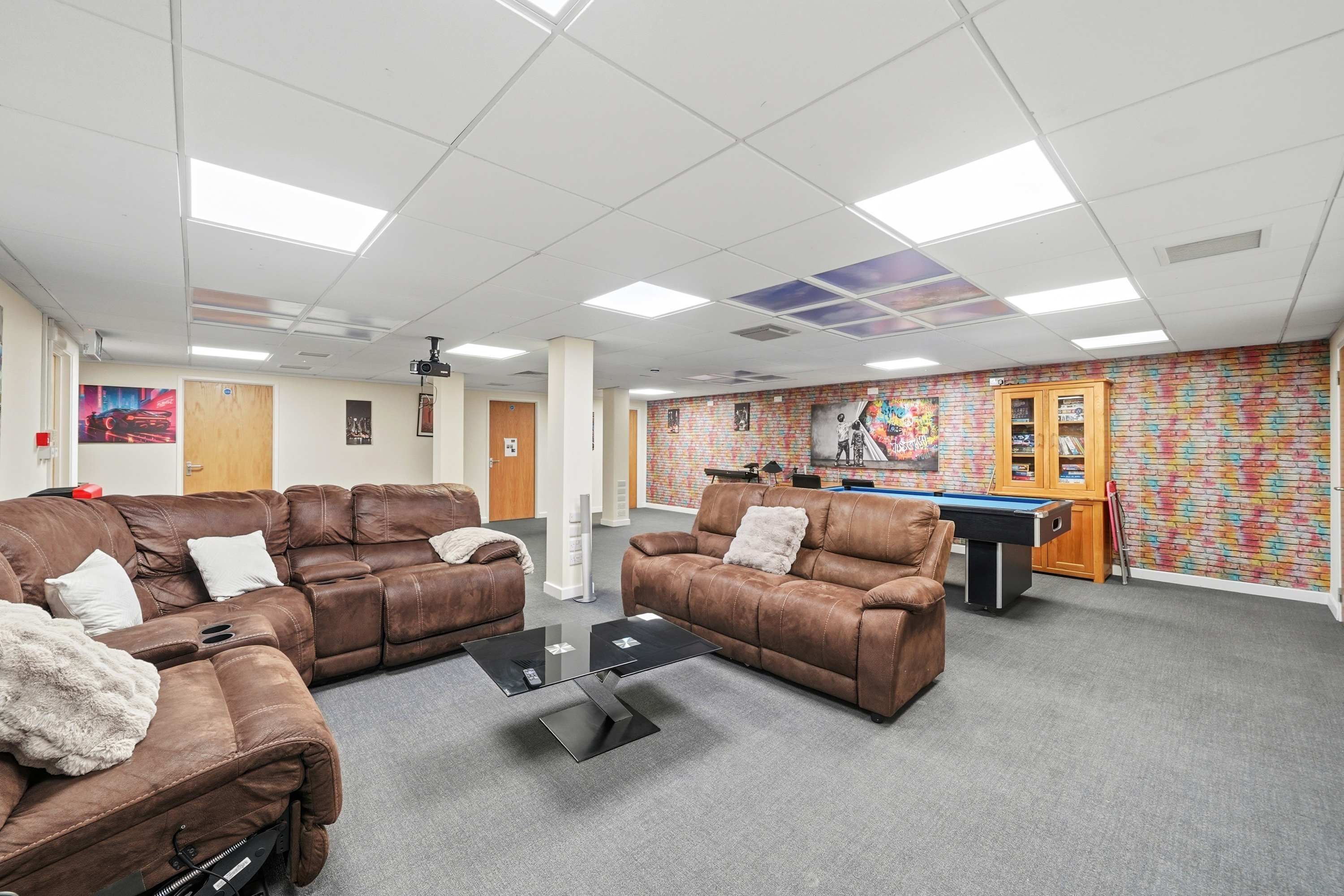 A room with brown leather sofas, a pool table, and a colorful wall mural.