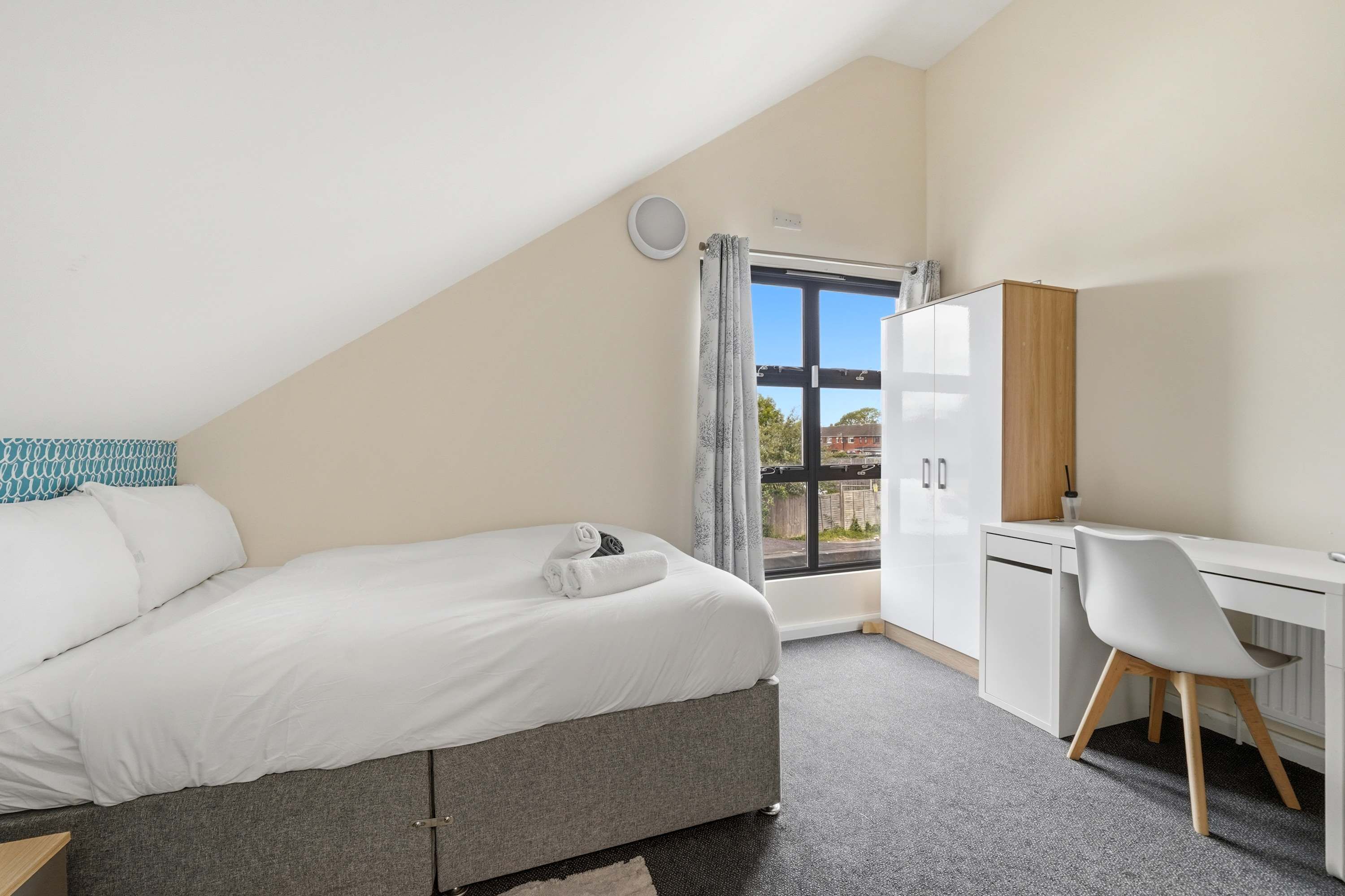 A bedroom with a bed, a desk, and a view through a window.