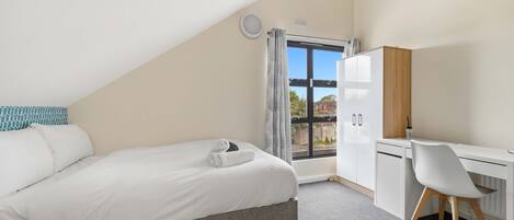 A bedroom with a bed, a desk, and a view through a window.