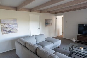 A modern living room with a grey sectional sofa, a glass coffee table, and a flat-screen TV. - Serene Family Retreat - Relax in Modern Comfort (Melbourne)