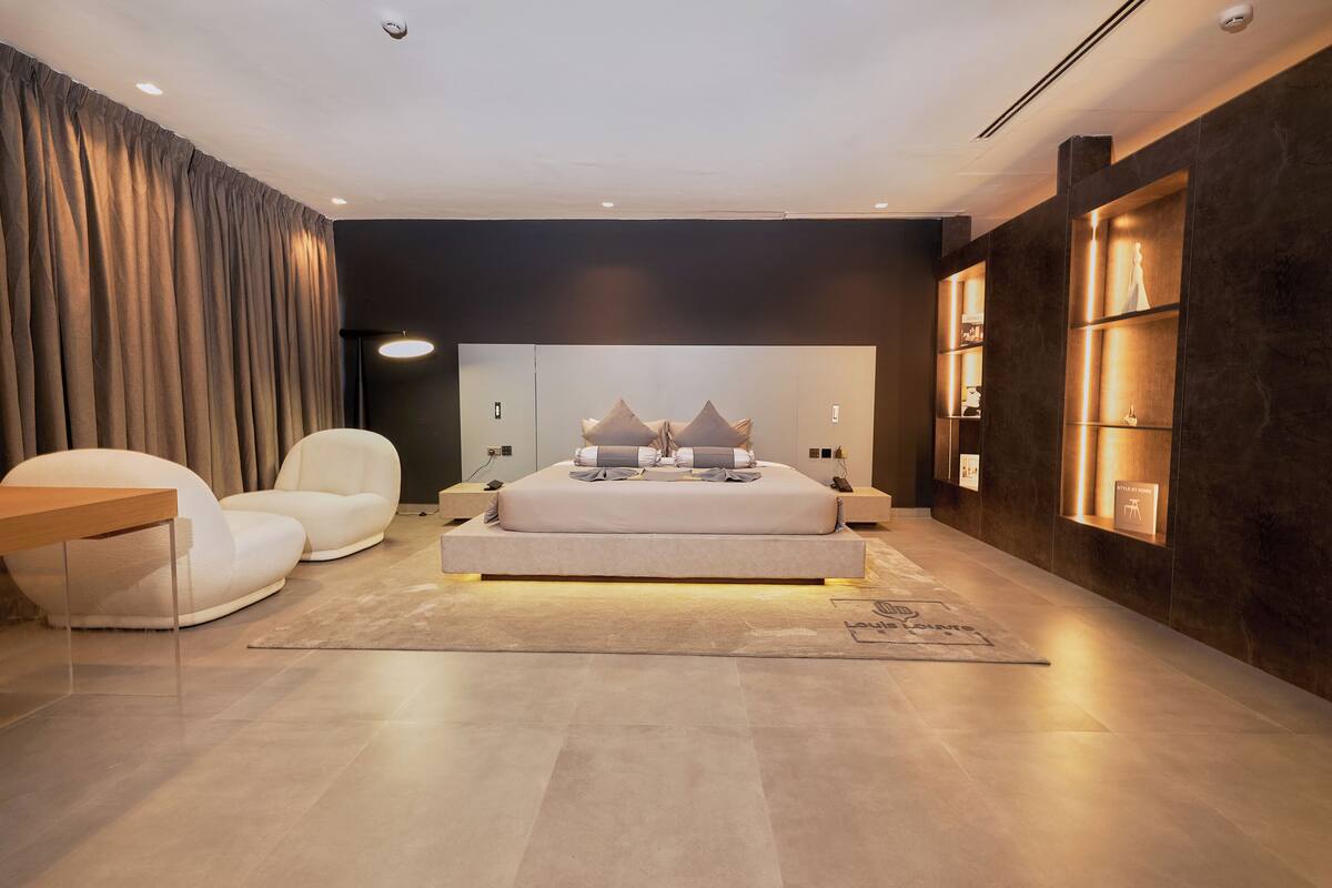 A modern bedroom with a large bed, a sofa, a desk, and built-in shelves.
