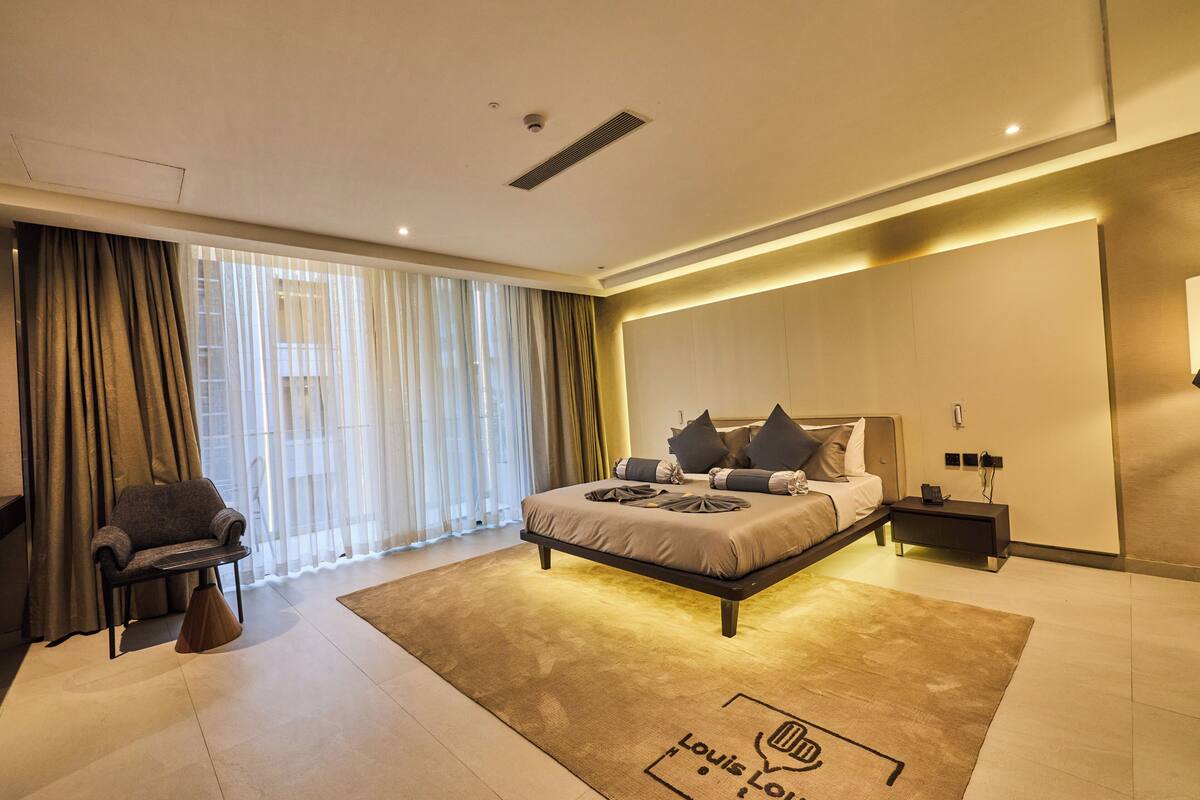 A modern bedroom with a bed, bedside tables, a chair, and a large window with curtains.