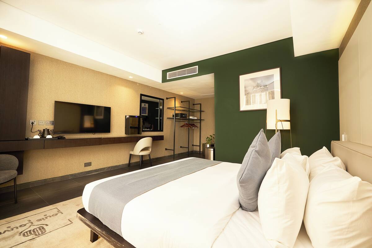 A hotel room with a bed, a desk, a chair, a TV, and a wall-mounted shelf.