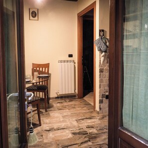 A narrow hallway with a stone floor, a wooden chair, a table, and a radiator.