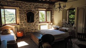 A rustic bedroom with a stone wall, a bed with ornate headboard, a chest of drawers, a nightstand, and a chandelier.
