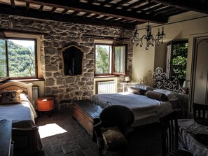 Ein rustikales Schlafzimmer mit Steinwänden, Holzbalkendecke, einem Bett mit Kopfteil, einer Bank und einem Stuhl.