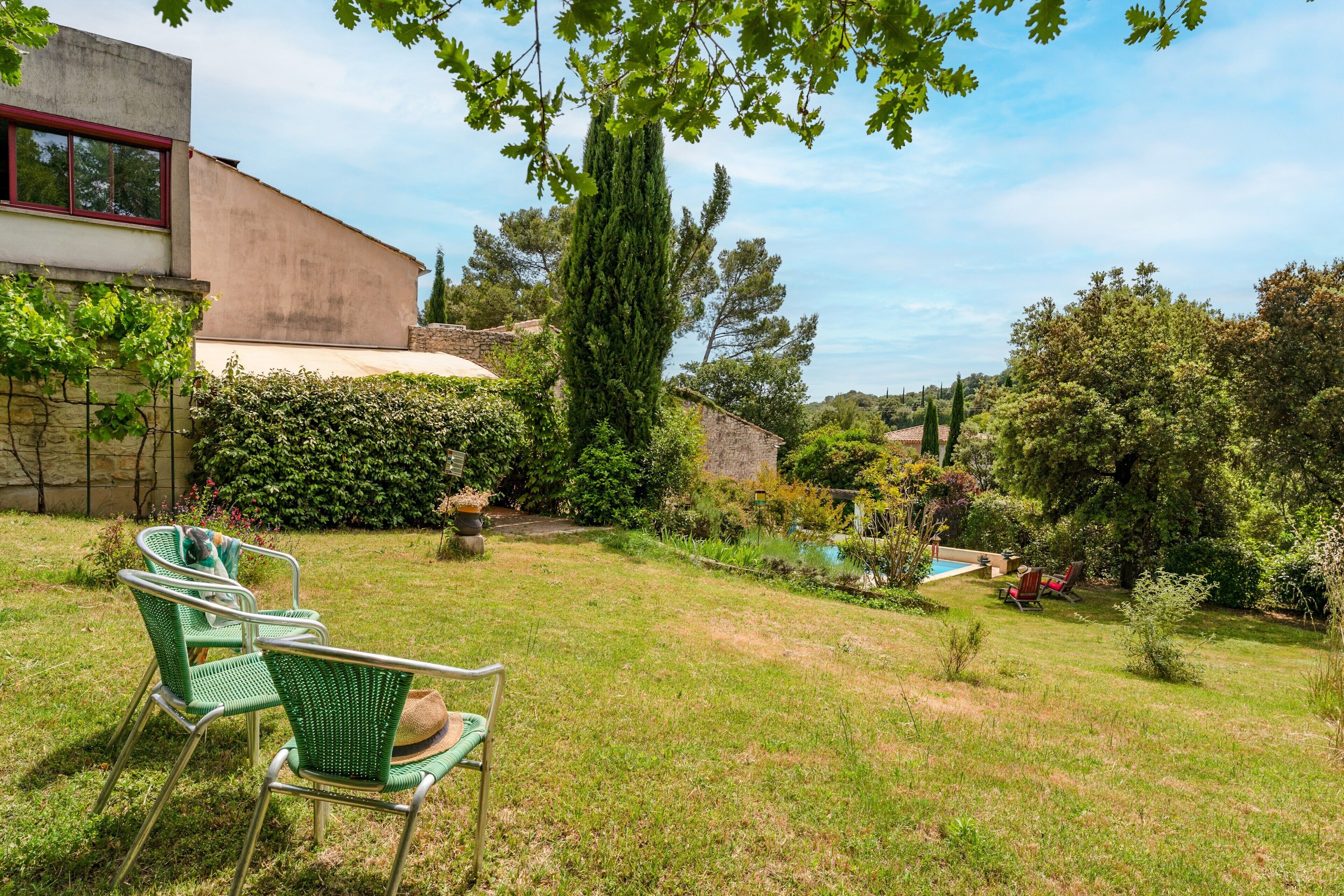 A backyard with a swimming pool, green chairs, and a tall tree.