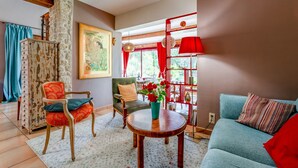 A living room with a sofa, chairs, a table, a vase with flowers, a painting, and a red lamp. - Coquelicot Guest Room with Shared Pool, Wi-Fi, and Air Conditioning (Lagarde-Paréol)