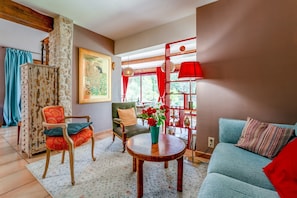Ein Wohnzimmer mit einer Couch, Stühlen, einem Tisch, einer Vase mit Blumen, einem Gemälde und einer roten Lampe.