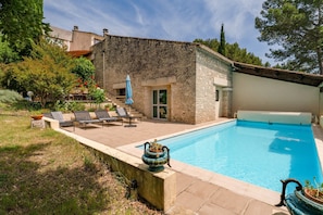 Ein Swimmingpool mit Liegestühlen, ein Steinhaus und ein Garten.