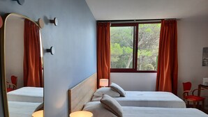 A hotel room with two beds, a large mirror, a window with curtains, and a lamp. - Orchidée Guest Room with Shared Pool, Wi-Fi, and Air Conditioning (Lagarde-Paréol)