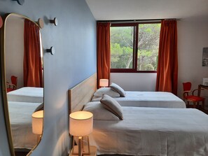 Hotellihuone, jossa on kaksi sänkyä, suuri peili, ikkuna verhoilla ja lamppu.
