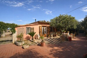 Ein eingeschossiges Haus mit Pflasterterrasse, Holzzaun und Kübelpflanzen.