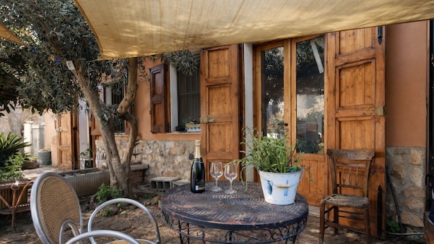 Une terrasse extérieure avec une table ronde en métal, deux chaises, une plante en pot et une bouteille de vin.
