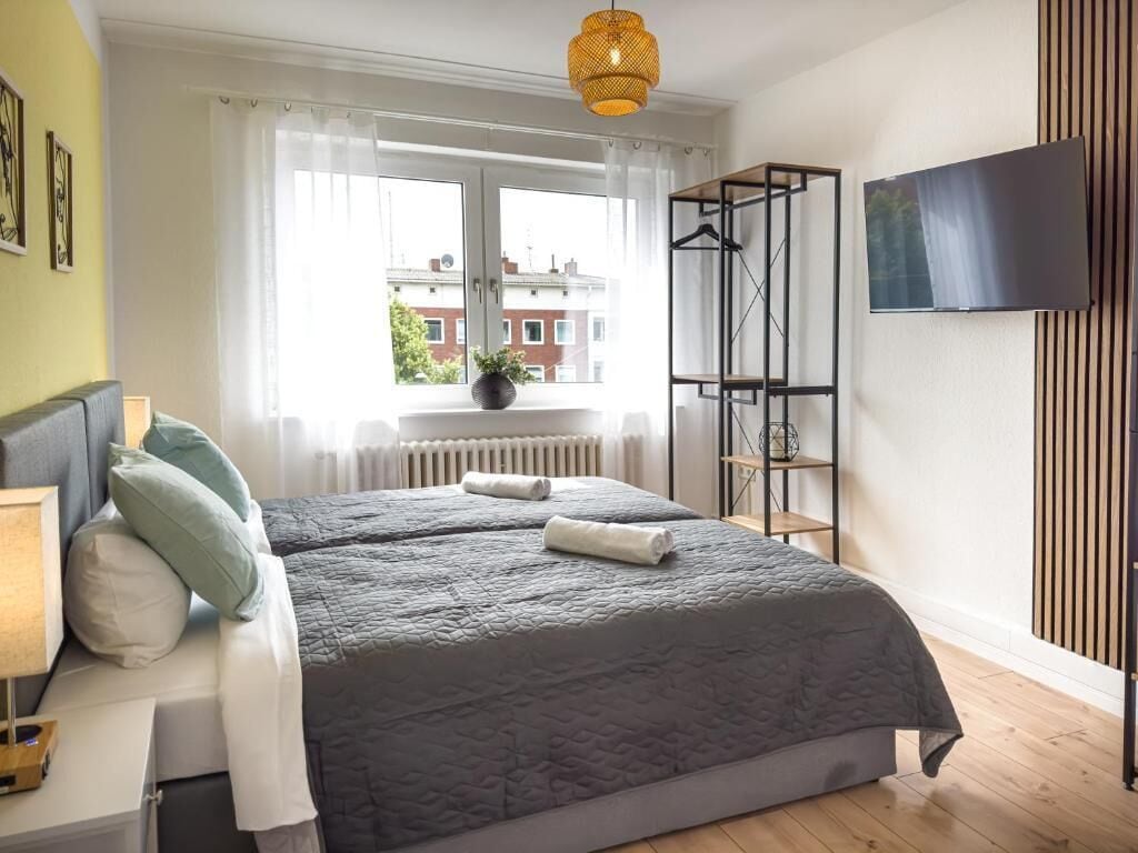 A bedroom with a bed, a TV, a window with curtains, and a radiator.