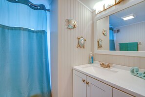 Ein Badezimmer mit Duschvorhang, Waschbecken und einem Spiegel, sowie dekorativen Wandbildern.