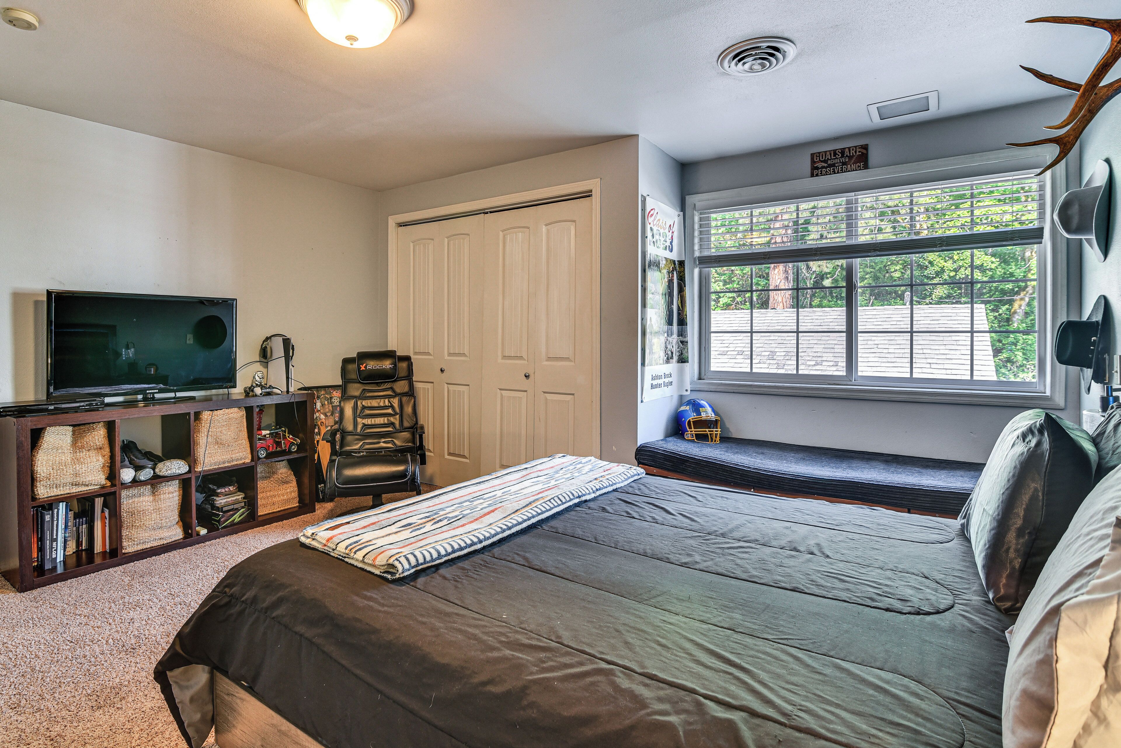 A bedroom with a bed, a television, a bookshelf, a window with a view, and a door.