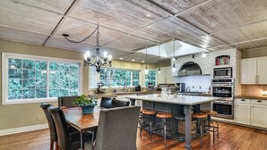 A kitchen with a large island, wooden flooring, and a view of trees through the windows.