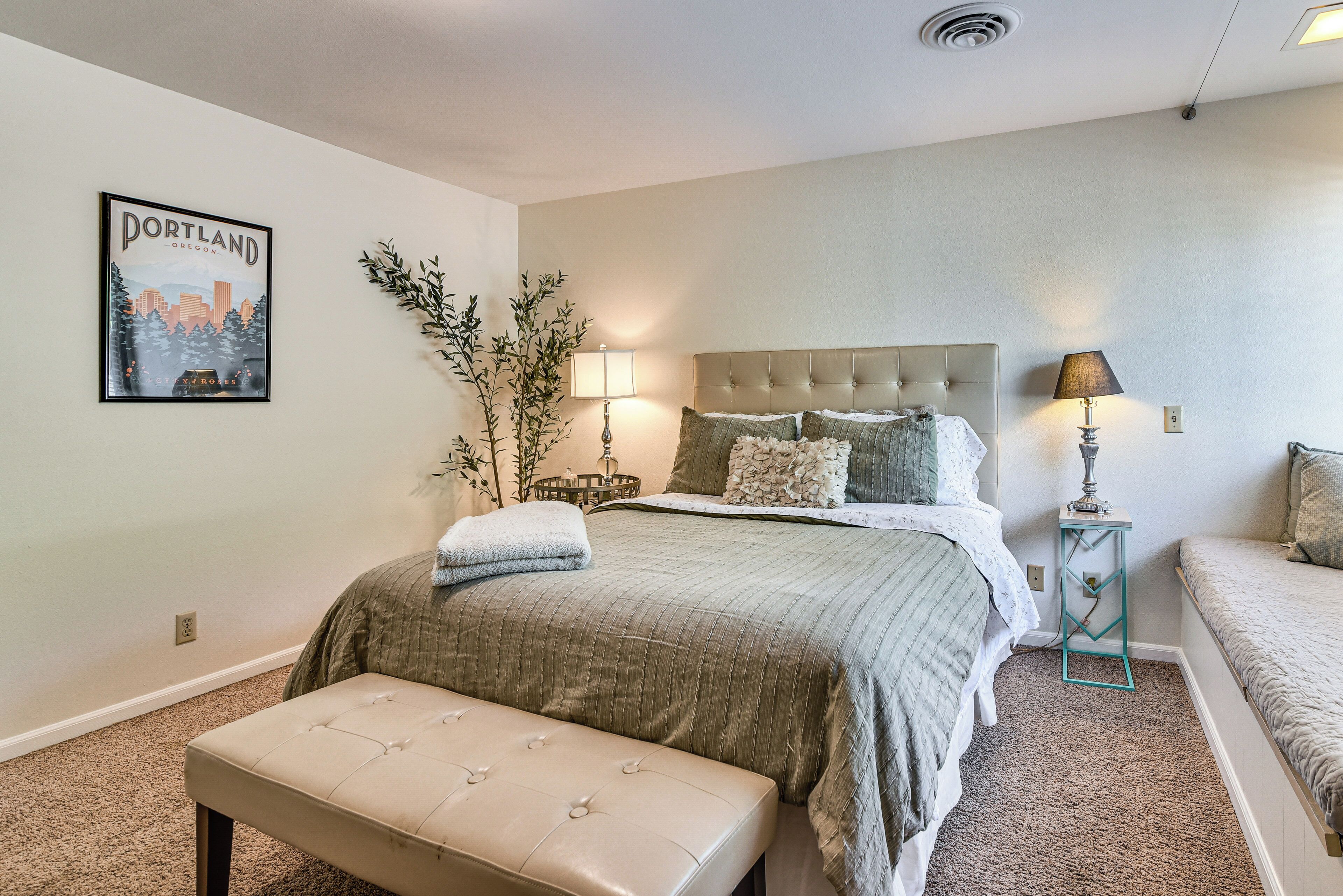 A bedroom with a bed, bedside tables, a bench, a wall-mounted lamp, and a poster.