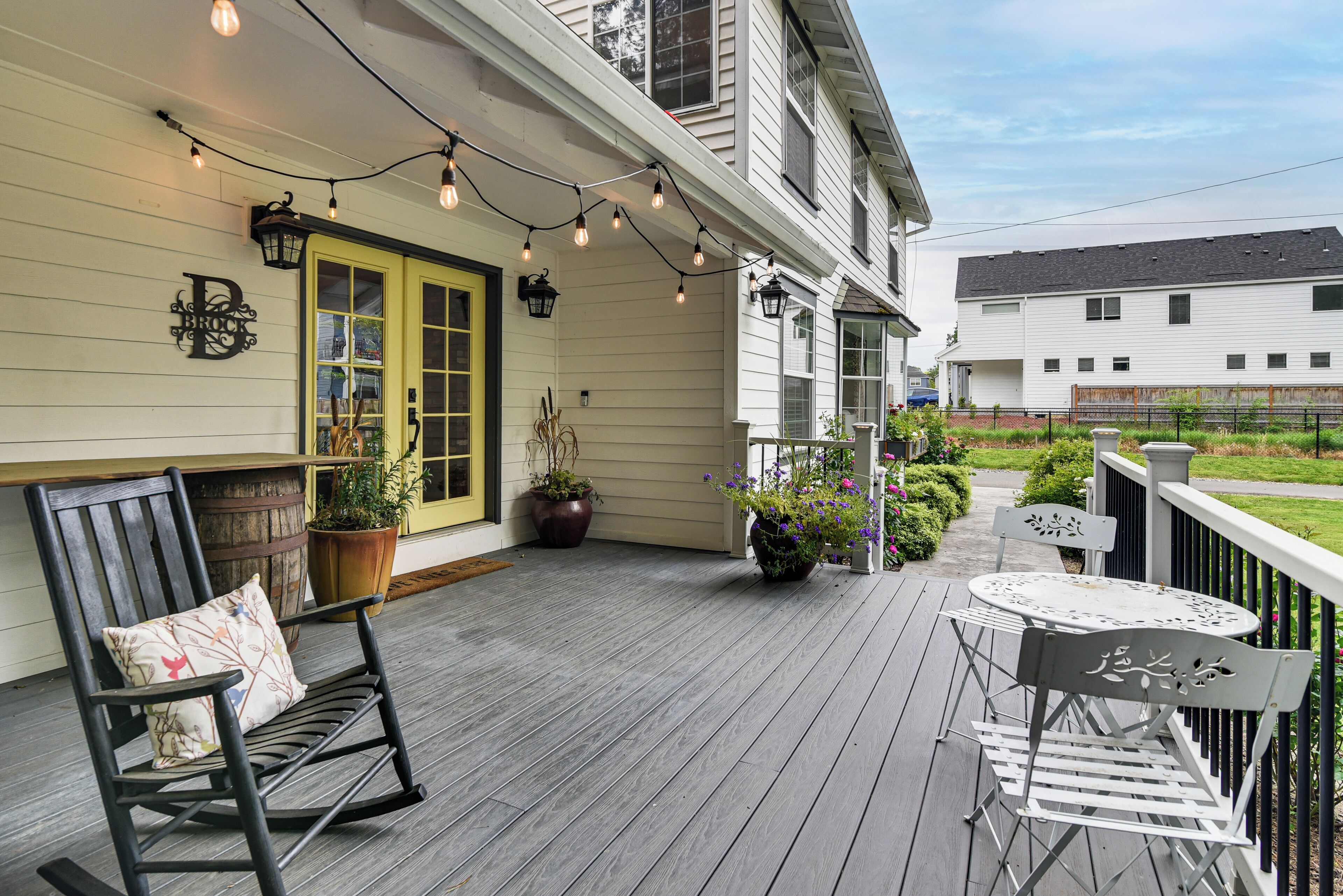 A wooden deck with outdoor furniture, string lights, and potted plants.