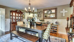 A dining area with a wooden table, benches, a chandelier, a wine rack, and a mirror with a cross.