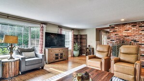 A living room with a TV, leather chairs, a wooden coffee table, and a brick wall.