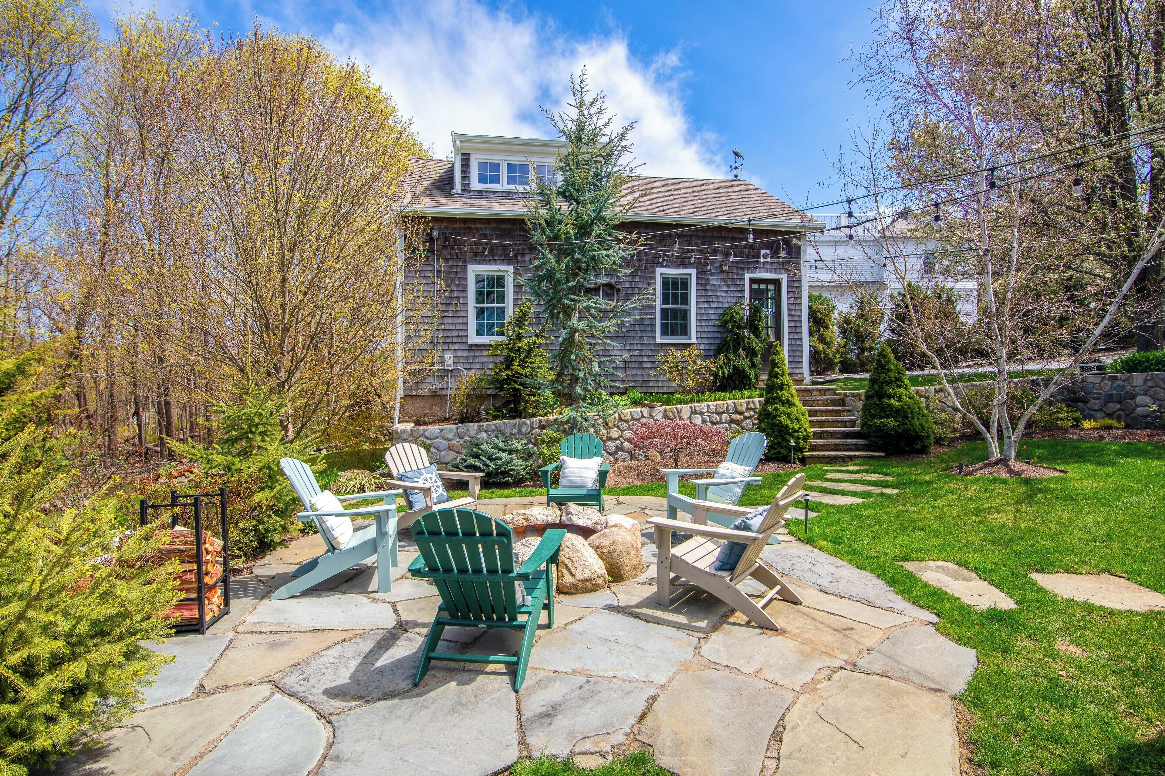 A stone patio with Adirondack chairs, a stone wall, and a house with a chimney.