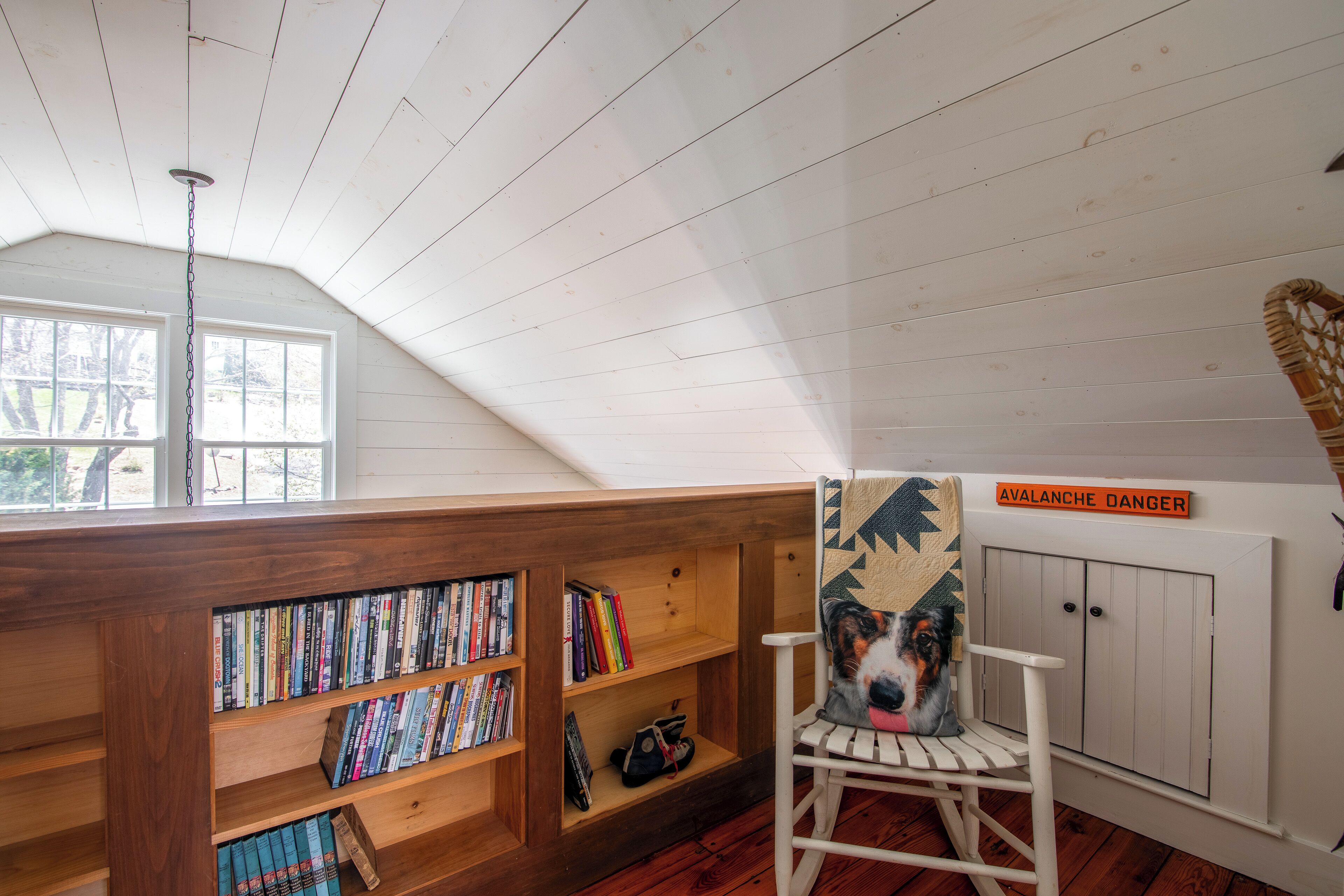 A cozy reading nook with bookshelves, a chair, and a sign reading 'Avalanche Danger'.