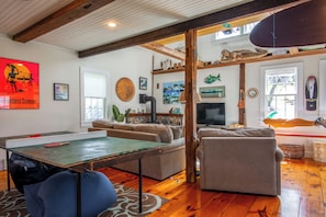 Quarto com mesa de ping pong, sofás, televisão e várias decorações, incluindo uma escultura de peixe e uma prancha de surf.