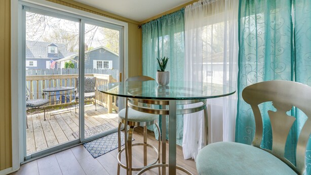 Een kamer met een glazen tafel, twee stoelen, een potplant en een schuifdeur naar een terras.