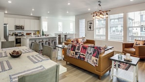 A modern kitchen with white cabinets, a dining area with a large table, and a cozy living space with a sofa and chairs. - Pets Welcome! Thornton Extended Stay w/ Balcony (Thornton)