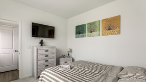 A bedroom with a bed, a dresser, a nightstand, a TV, and three wall-mounted paintings. - Pets Welcome! Thornton Extended Stay w/ Balcony (Thornton)