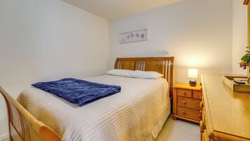 A bedroom with a bed, a wooden nightstand with a lamp, a dresser, and a wall-mounted picture.