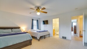 A bedroom with two beds, a ceiling fan, a TV, and a bathroom door. - Fire Pit & Grill! Spacious Port Huron Home By Dtwn (Port Huron)